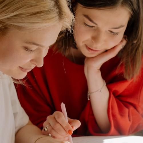 Two women look over a desk one with a pen in hand 