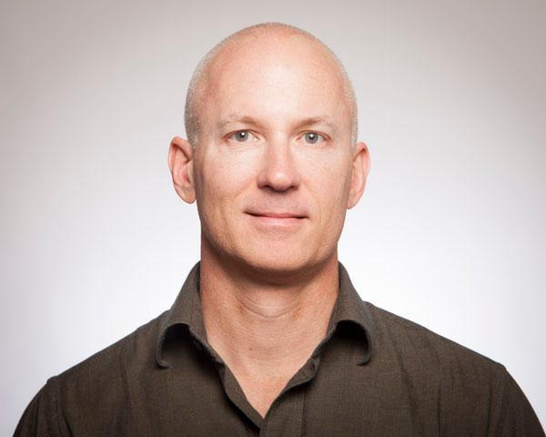 A man in a dark shirt against a plain background.