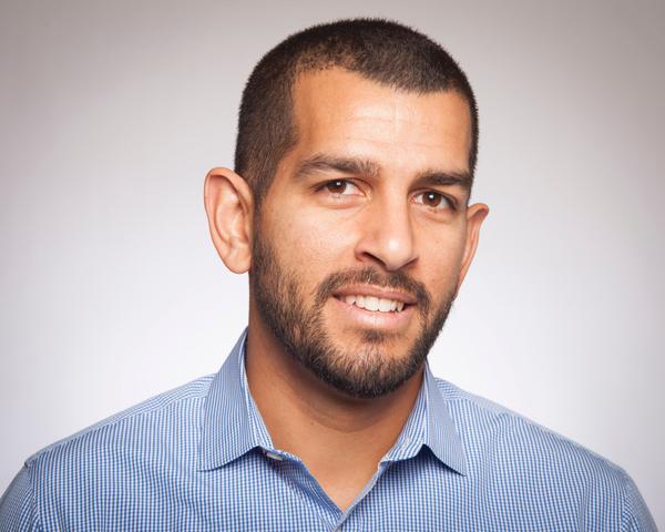 Andrew Ishak, smiling, wears a light blue shirt against a neutral background.
