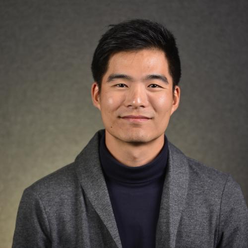 Man in a gray jacket and dark shirt smiling.