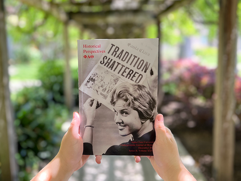 Hands holding a book under the SCU wisteria trellis.