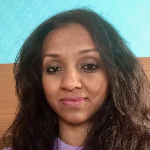 Smiling person in a purple top with a blue and brown background.