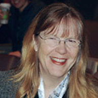 A smiling woman with glasses and long hair.