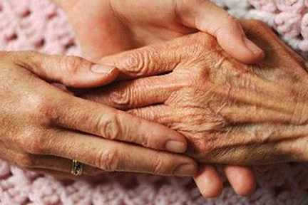 Two hands gently holding elderly hands, conveying care and compassion.