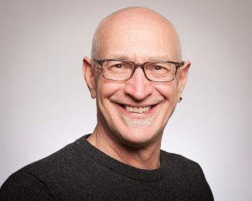 A person wearing glasses and a dark shirt smiling at the camera.