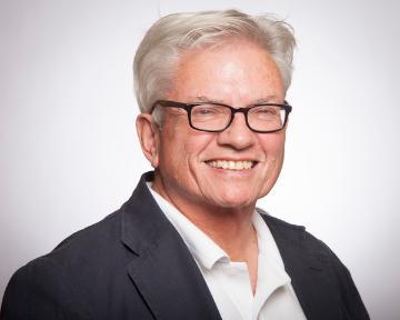 A man wearing glasses and a suit, smiling.