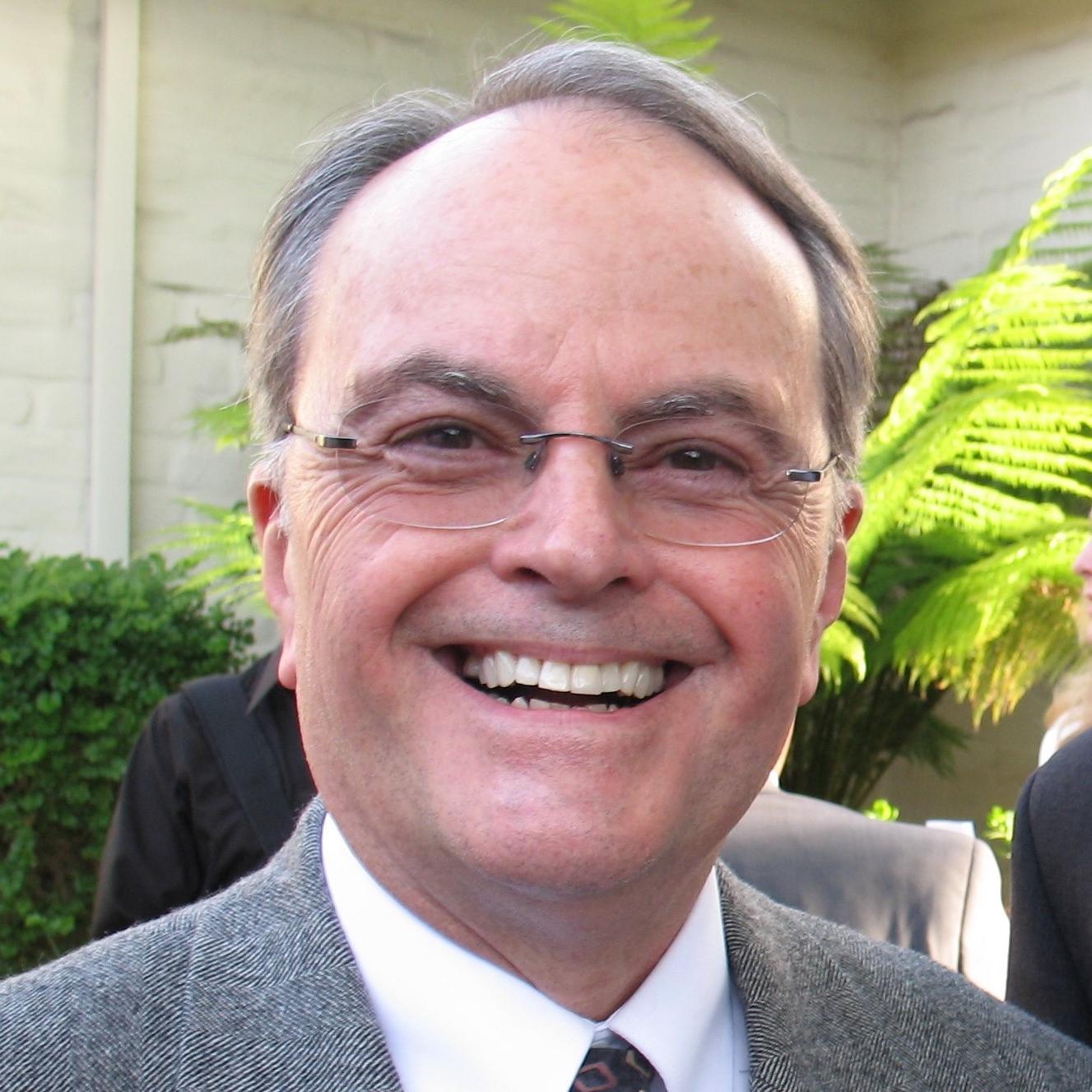 A man in a suit and tie smiling outdoors.