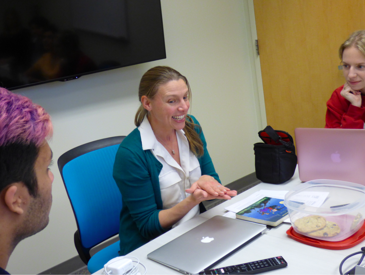 Three people sitting at a table with laptops and papers.