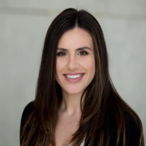 A woman smiling, wearing a white top and dark jacket.