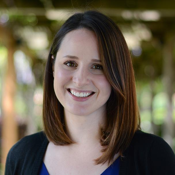 A person smiles outdoors with trees in the background.