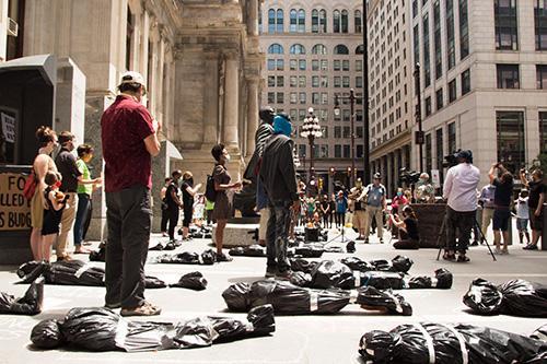 People gathering at Covid memorial in Philadelphia, with black bags on the ground.