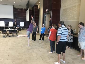 People during warm-up session in a large indoor space. Physics of Dance 2019d.