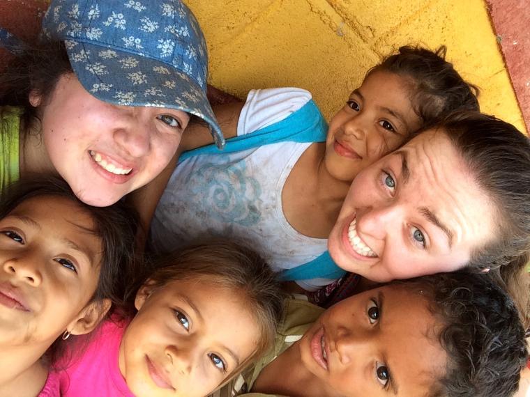 Group of smiling people huddled together under colorful fabric. 'Teatro Catalina 2015'.