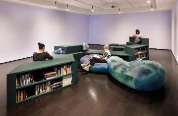People sitting on modular bookshelf and large cushions reading books 