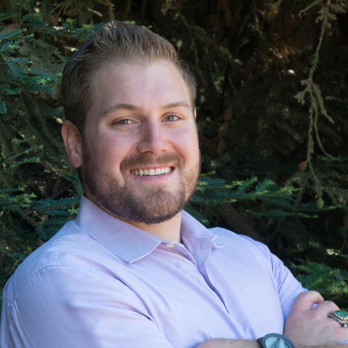 A headshot of Gregory Walswick with folded hands