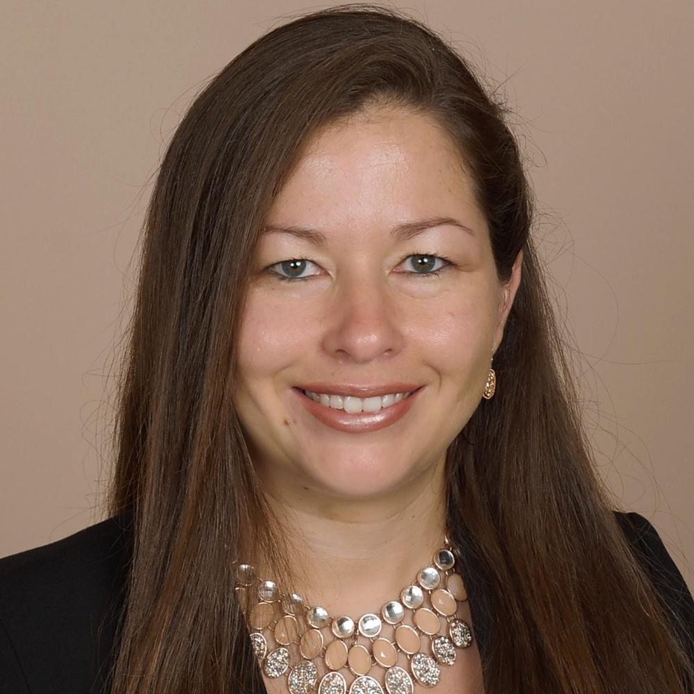 A woman smiling, wearing a necklace and a black top against a beige background.