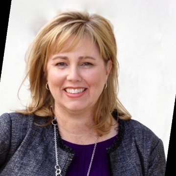A woman smiling, wearing a blazer and necklace. image link to story