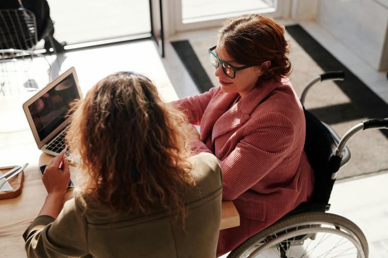 Woman in red sweater wearing black framed eyeglasses sitting on wheelchair. Photo by Marcus Aurelius/Pexels.
