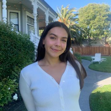 A person standing outside near a house and greenery.