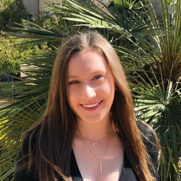A person smiling with greenery in the background.