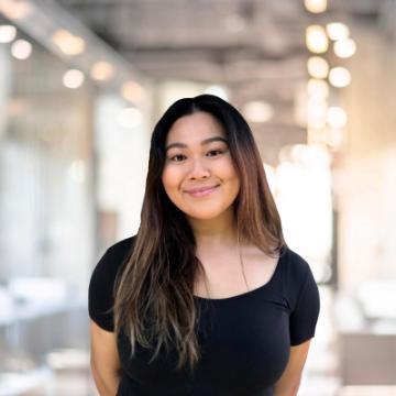 A person smiling in a well-lit room with blurred lights in the background.