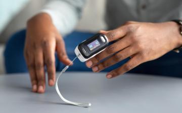 A close-up of a Black individual using a pulse oximeter on their fingertip.