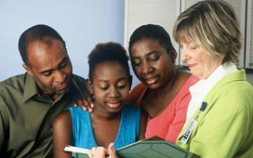 A Black female teenager and her parents consult with a female Caucasian doctor.