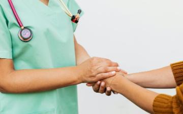 A medical professional in surgical clothing holds hands with a patient. Photo by Kaboompics.com via Pexels.