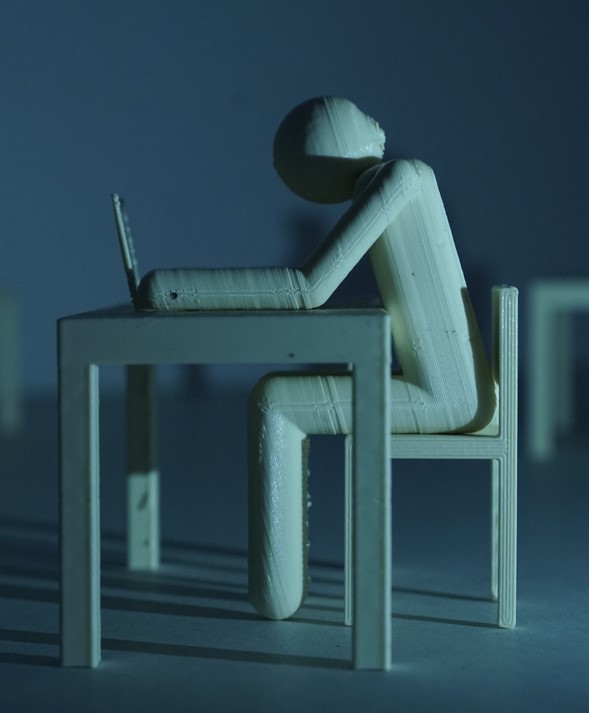 3D-printed figure working on a laptop at a desk.