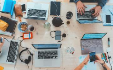 a work desk with laptops and electronics, coffee cups, notebooks, and personal items. 