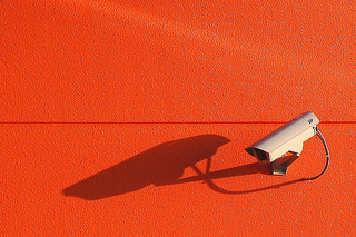 White surveillance camera mounted on an orange wall.