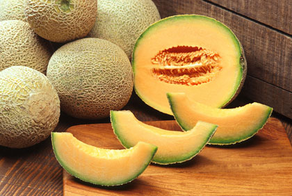 Fresh cantaloupe slices and whole cantaloupes on a wooden surface.