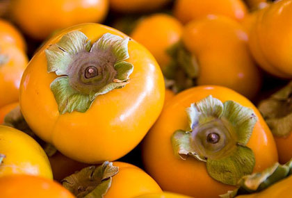 Bright orange persimmons with green tops piled together.