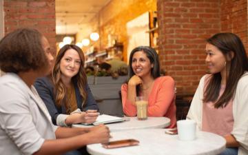 Four people engaged in a discussion around a table in an office setting. 