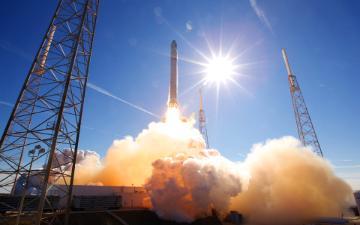 Rocket launching with smoke and flames under a clear blue sky.