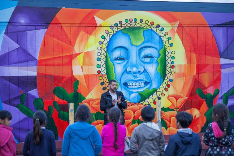 Colorful mural with a smiling face surrounded by children looking at it.