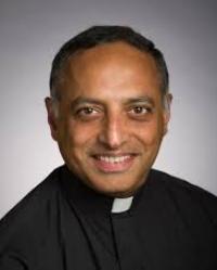 Nicholas Santos, S.J. smiling in a clerical collar and black shirt.