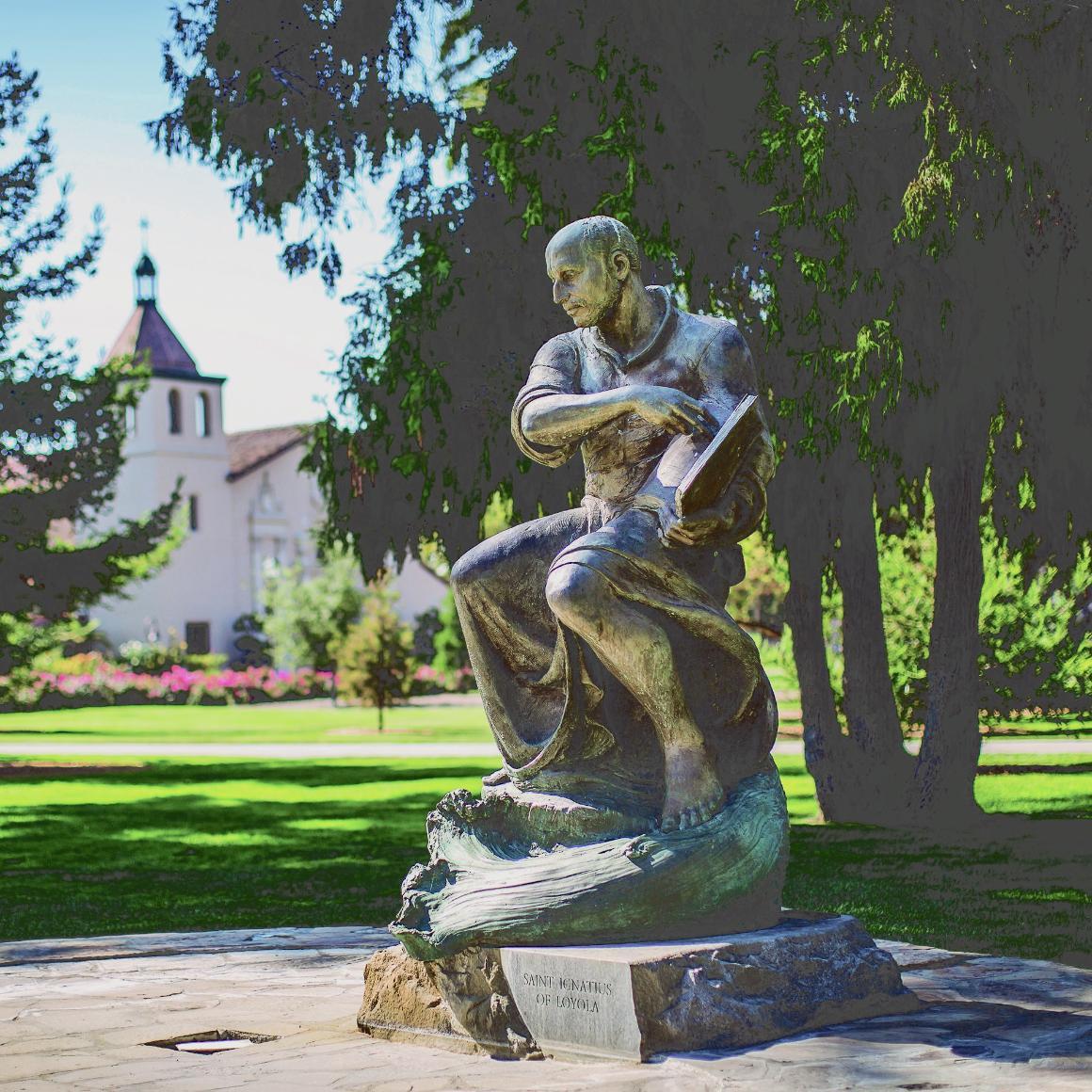 A statue in Ignatius Square with trees and a building in the background.