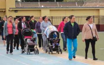 A group of people walking with strollers on a sports track.