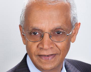 Headshot of a man wearing glasses and a suit against a plain background.
