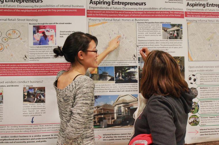 Two women discussing a wall display titled The Greater Washington Report.