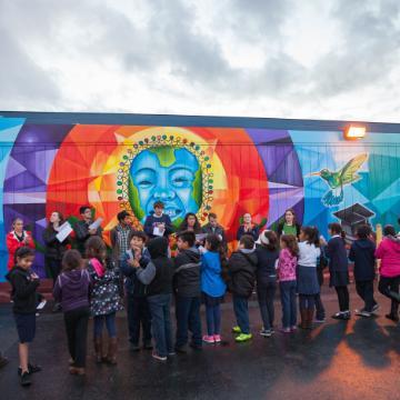 A large group of people stands in front of a colorful mural.