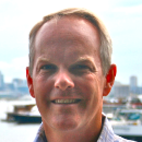 A person smiling in front of a marina.