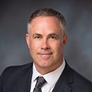 A man in a suit and tie with a grey background.