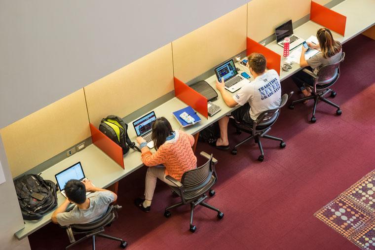 People studying at desks with laptops in a library.