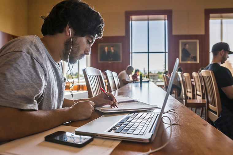 People studying with laptops and books at a library table.