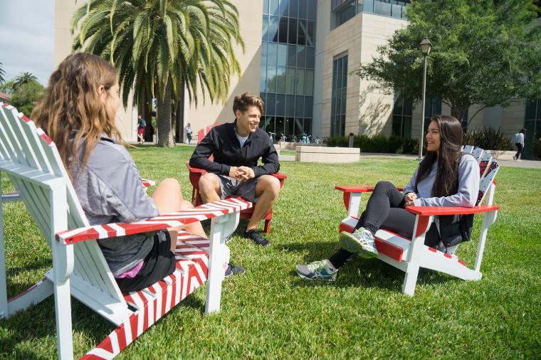 Three people sitting on chairs outside near a building.
