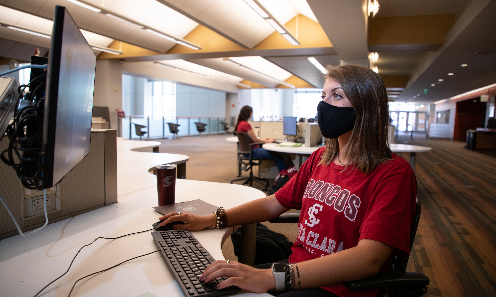 A student wearing a mask uses a computer in a library. image link to story