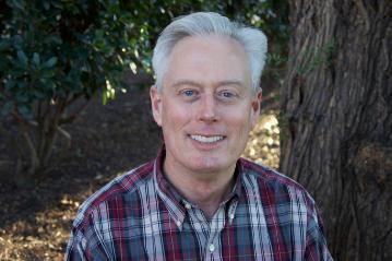 A man in a plaid shirt smiling outdoors.