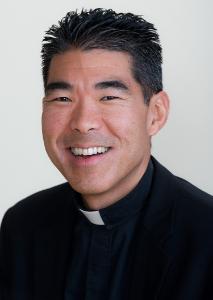 A clergyman smiling with a white background.